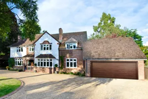 A large detached property with a garage attached with a brown sectional garage door and a shingle driveway.