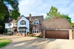 A large detached property with a garage attached with a brown sectional garage door and a shingle driveway.