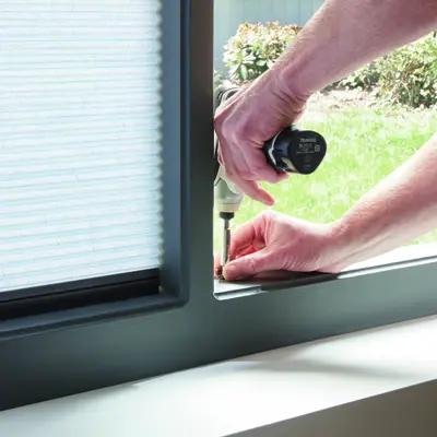 An installer screwing a blind fitting into a frame.
