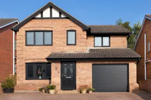 Contemporary house with apex window and integral garage with black roller garage door that matches the black front door and red block paving driveway.