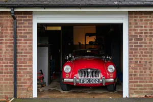 Red brick garage with white door partially raised to show a red MG sports car.