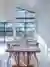 Dining area with contemporary wooden table and chairs set in front of two large windows beneath a mezzanine shaped window dressed in blue duette blinds.