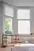 White coloured blinds fitted to bay shaped windows in a spacious study room with a desk, chair, footstool and circular rug 