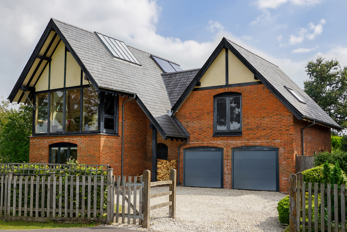 Large house with attached garage and second storey block with two grey sectional garage doors.