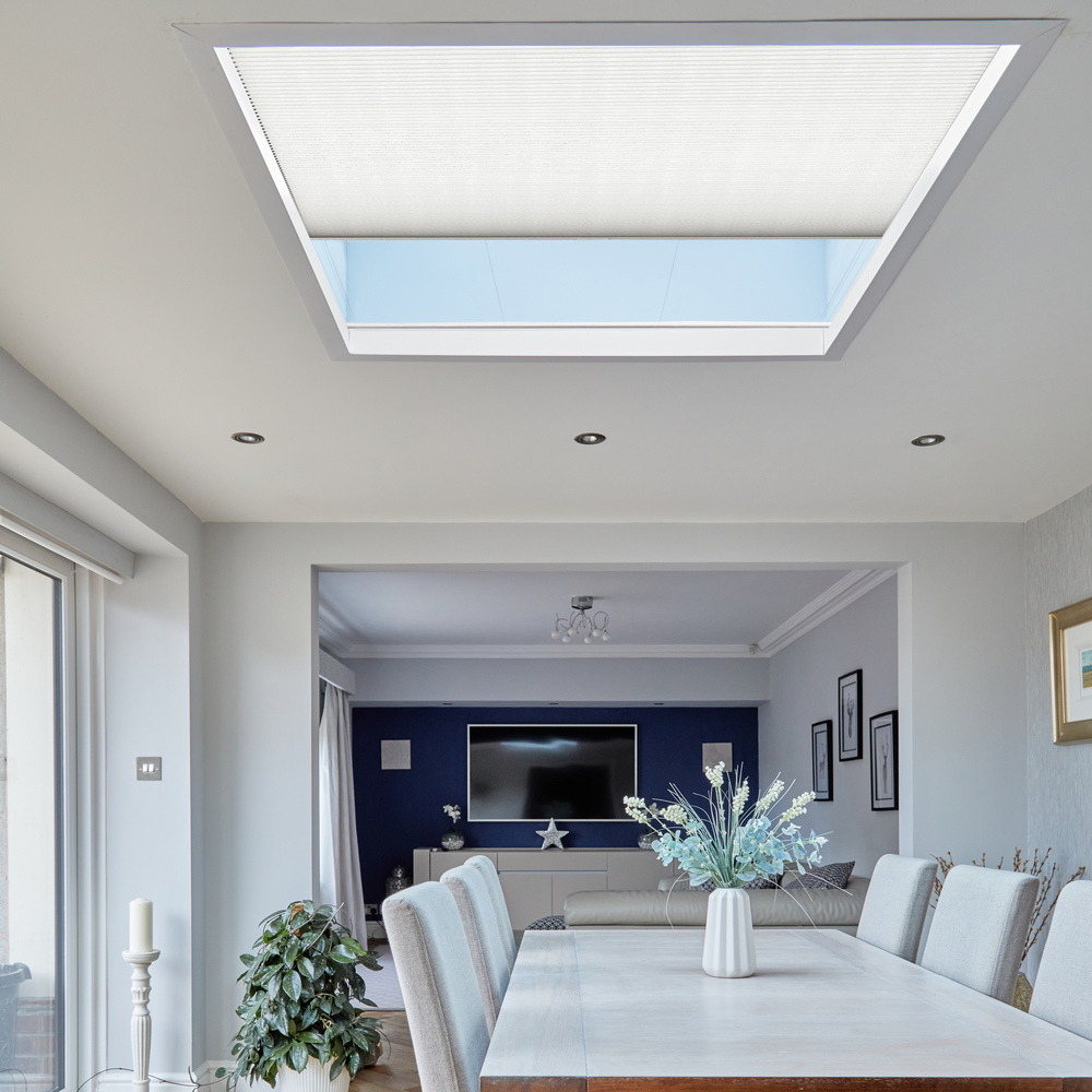 Dining room with roof lantern window dressed in white duette blind partially open, wood table with white top, white chairs and parquet floor.
