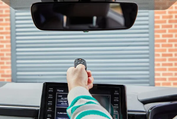 A person opening a garage door with an electric key fob from their car.