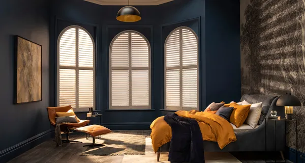White arch shaped shutters fitted to arch windows in a bedroom decorated in blue, grey and yellow