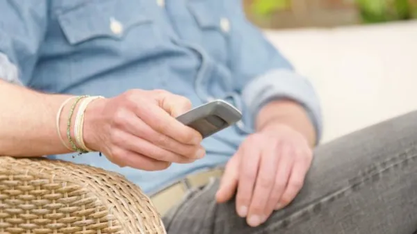 Close up of man in a wicker chair outdoors clicking a button on a remote control.