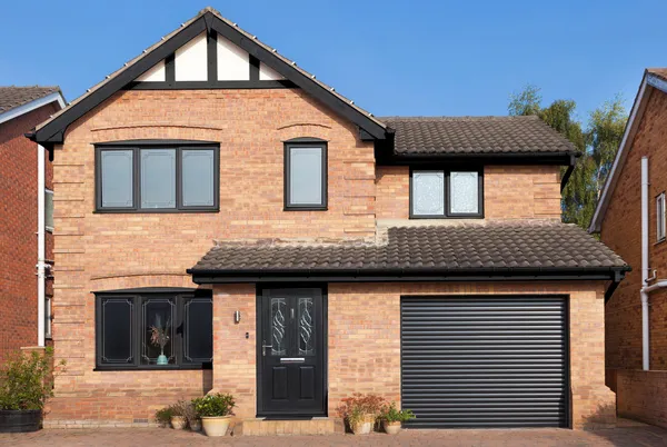 Contemporary house with apex window and integral garage with black roller garage door that matches the black front door and red block paving driveway.