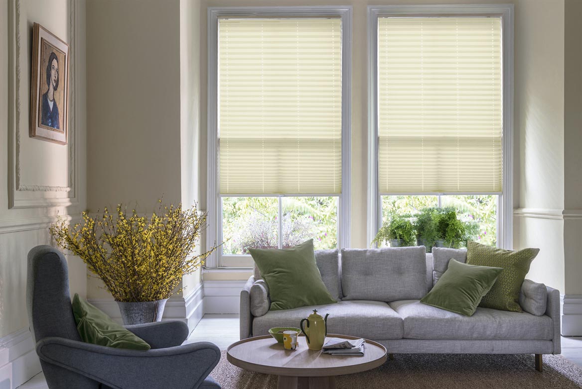 natural Parchment Warm Stone Crush Pleated blind are fitted to a series of windows in a kitchen decorated with marble counter tops, white walls and drawers. The Pleated blinds are decorated in a plain style.