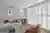  Grey ounge with full wall of white tracked shutters floor to ceiling louvres open, grey sofa terracotta cushions background, upholstered gold velvet chair foreground, a glass circular coffe table in between.