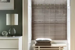 Room with dark olive walls and cream accessories with a small cream radiator at an inset window dressed in a dark wood venetian blind, fully lowered.