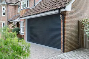 Beige brick townhouse style property with integral garage and garage door in dark grey matching the front door and window frames.
