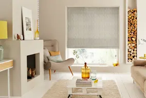 Neutral lounge with fireplace to left, rug on white wood floor in centre with wheeled pallet table and chartreuse glassware, corner chair by window which is dressed with beige-grey Roman blind with vertical zigzag pattern.