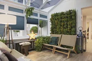 Conservatory with wooden floor and windows dressed in azure blue duette blinds, raffia chairs, large standard lamp with cream shade, greenery wall.