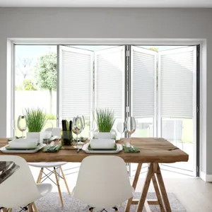 Dining room in pale grey with pale wood floor, wooden trestle-style table with white contemporary chairs, table set with white crockery and bifold doors dressed with white blinds within frame, doors partially open.