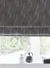 Close up of window with Roman blind in deep grey with dense pattern, dark and pale grey accessories on window sill.