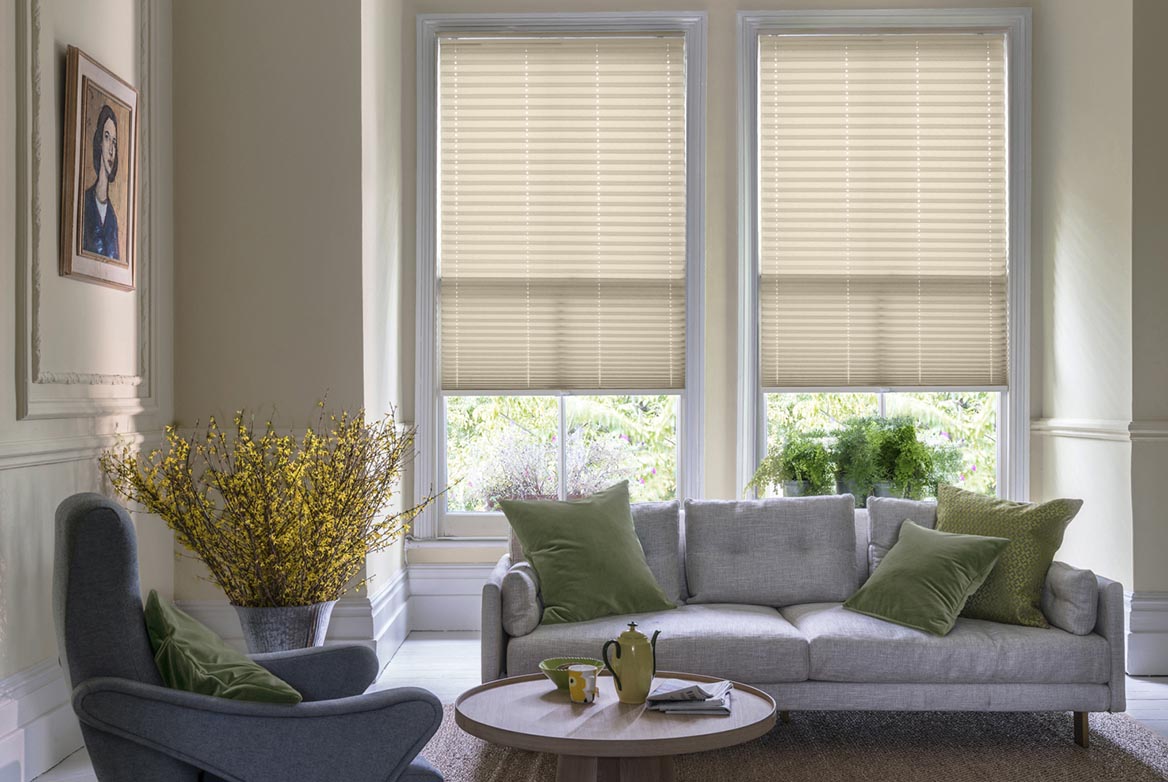 natural Solartex Chintz Ivory Crush Pleated blind are fitted to a series of windows in a kitchen decorated with marble counter tops, white walls and drawers. The Pleated blinds are decorated in a plain style.