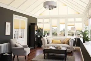 Conservatory with dark wood floor, cream sofa and chairs, dark wood coffee table with windows, doors and roof dressed in ivory duette blinds, window blinds at varying heights with roof blinds closed..