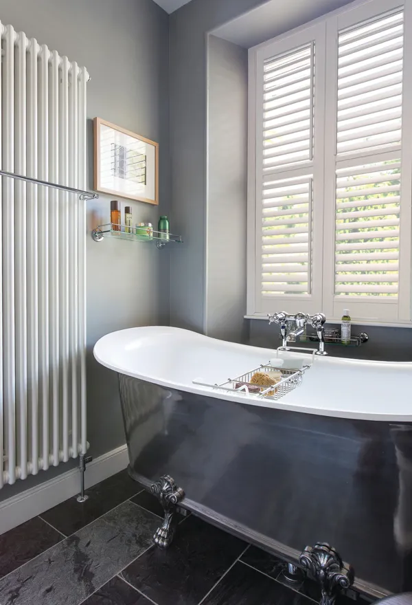 white shutters in bathroom with vertical radiator and a bath with a navy blue outside