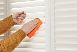 White shutters with louvres being wiped with an orange cloth.