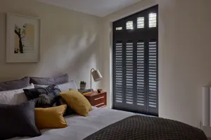 Bedroom that has white, chartreuse and charcoal bed linen with a black shutter and a second black shaped angled shutter to the top.