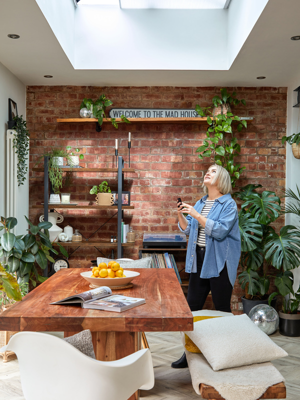 Dining area with rustic wooden table and benches underneath a roof lantern window, a woman with mobile in hand looks up.
