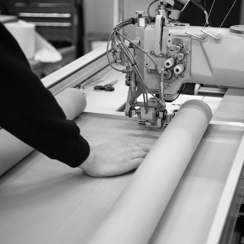 Black and white image of a man using an industrial sewing machine to make an awning in a factory.