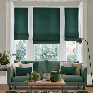 dark green roman blind in large full height living room window in between two thinner matching romans behind green sofa and light brown coffee table
