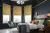 Large bedroom with wooden floor, navy walls, bed with white bedding and grey quilted throw, modern pendant light, bay window with three ochre faux velvet Roman blinds.