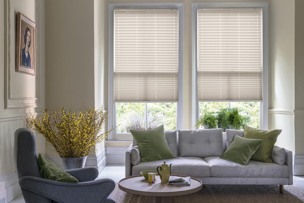 ivory Solartex Chintz Barley Pleated blind are fitted to a series of windows in a kitchen decorated with marble counter tops, white walls and drawers. The Pleated blinds are decorated in a plain style.