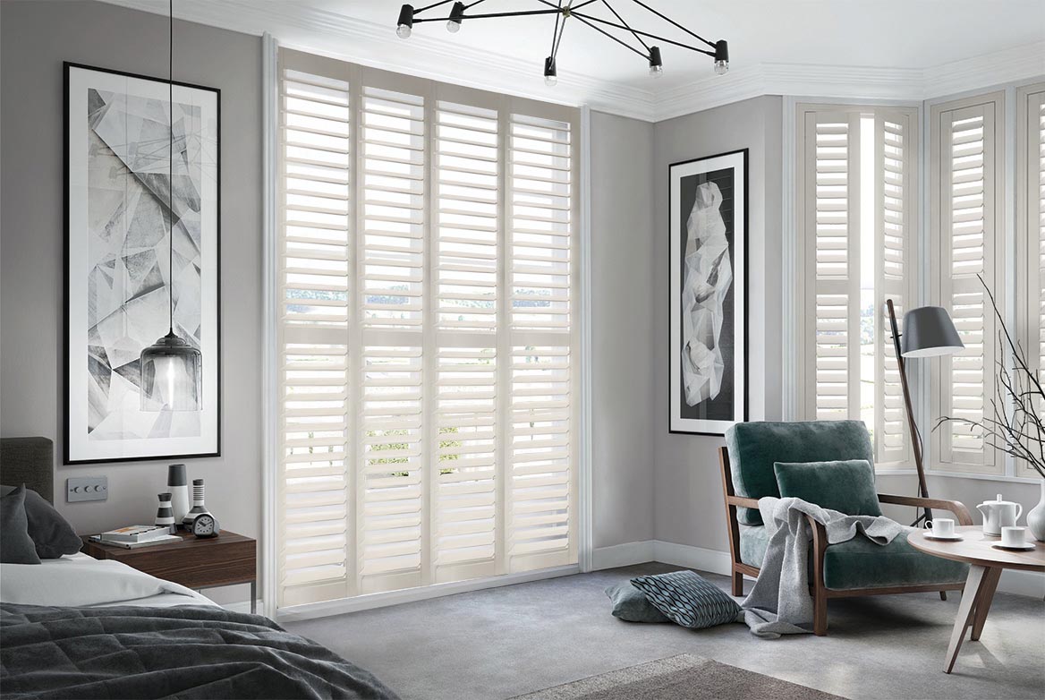 On a series of tall windows Mellow Olive Shutters have been fitted. The Ivory colour suits the bedroom which is decorated in grey and wooden tones.