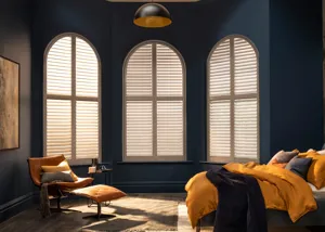 Navy bedroom with three arched windows dressed in white shutters, bed with mustard and navy bedding to right.