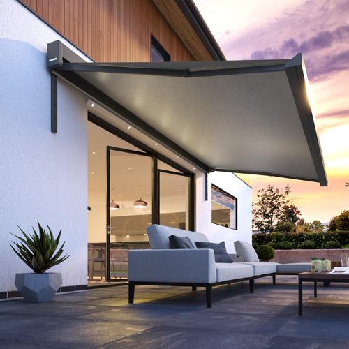 Evening shot of contemporary split level house with patio at bifold doors with grey awning extended over.
