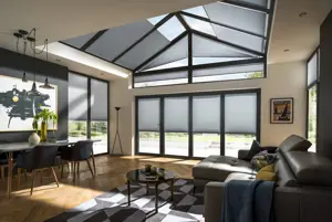 Open plan lounge diner with gable end and roof lantern windows and doors dressed in pale grey duette blinds, parquet floor, chocolate brown sofas on right, dining table and chairs on left with a geometric white and dark grey patterned rug in the middle.