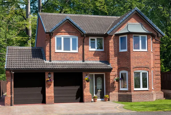 Large traditional brick house with apex windows and two internal garages with dark brown roller doors that match the front door.