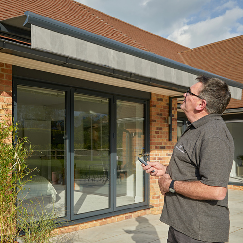 Exterior of house where an installer watches an awning extend using a remote control.