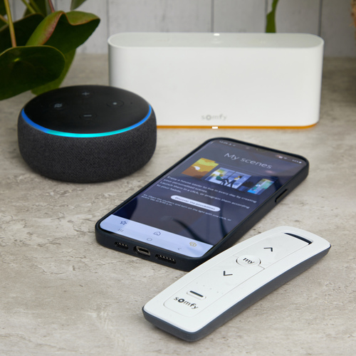Smart hub, Amazon Echo Dot, mobile phone and remote control sitting on a marble counter.