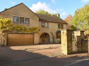 Large Yorkshire-style stone house and drive with integral garage door in mid brown matching front door, with climbing plant above garage.