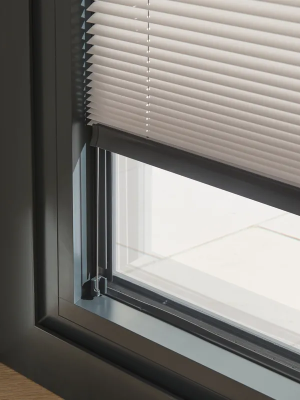 Close up of the bottom of a dark brown sliding door frame dressed with an ivory pleated blind lowered just short of the frame.