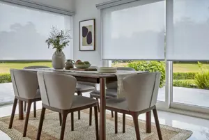 Close up of dining table and chairs on jute rug over ceramic tiled floor with doors and windows dressed in white roller blinds.