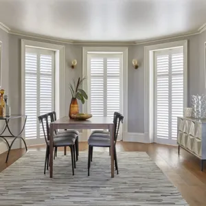 full height white shutters in a dining room with a large light rug and dark dining room table