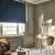 Home office with window dressed in navy velvet Roman blinds, half lowered., tan chair, desk and tan upholstered chair.