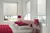 White bedroom with pale cream Duette blind at three windows, bed with white bedding with cerise throw, cushions and matching table lamps.
