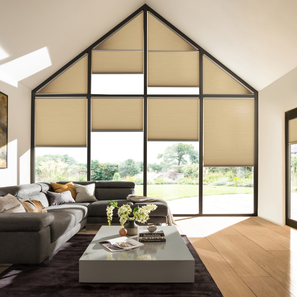 Gable end windows and doors in living room with buttermilk walls, brown sofa, grey low table, wood floor, French doors on right hand wall, all windows and doors dressed in pale caramel Duette blinds at varying heights.