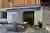Exterior of split render and wood panel housewith grey striped awning extended over wooden table and benches set for meal, cushions and throws on bench.