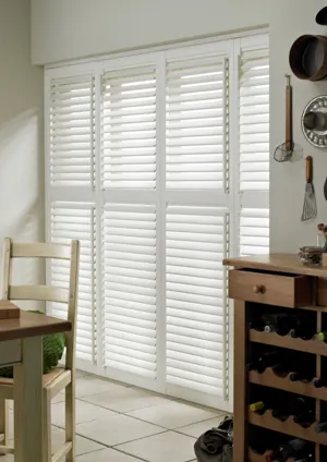 White tiered shutters fitted to a tall door window in a kitchen decorated with white walls