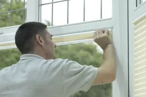 A blinds installer fits an ivory pleated blind into a bay window.