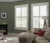 Living room with olive green walls, beige sofa and two large windows dressed in white shutters, louvres open.