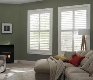 Living room with olive green walls, beige sofa and two large windows dressed in white shutters, louvres open.